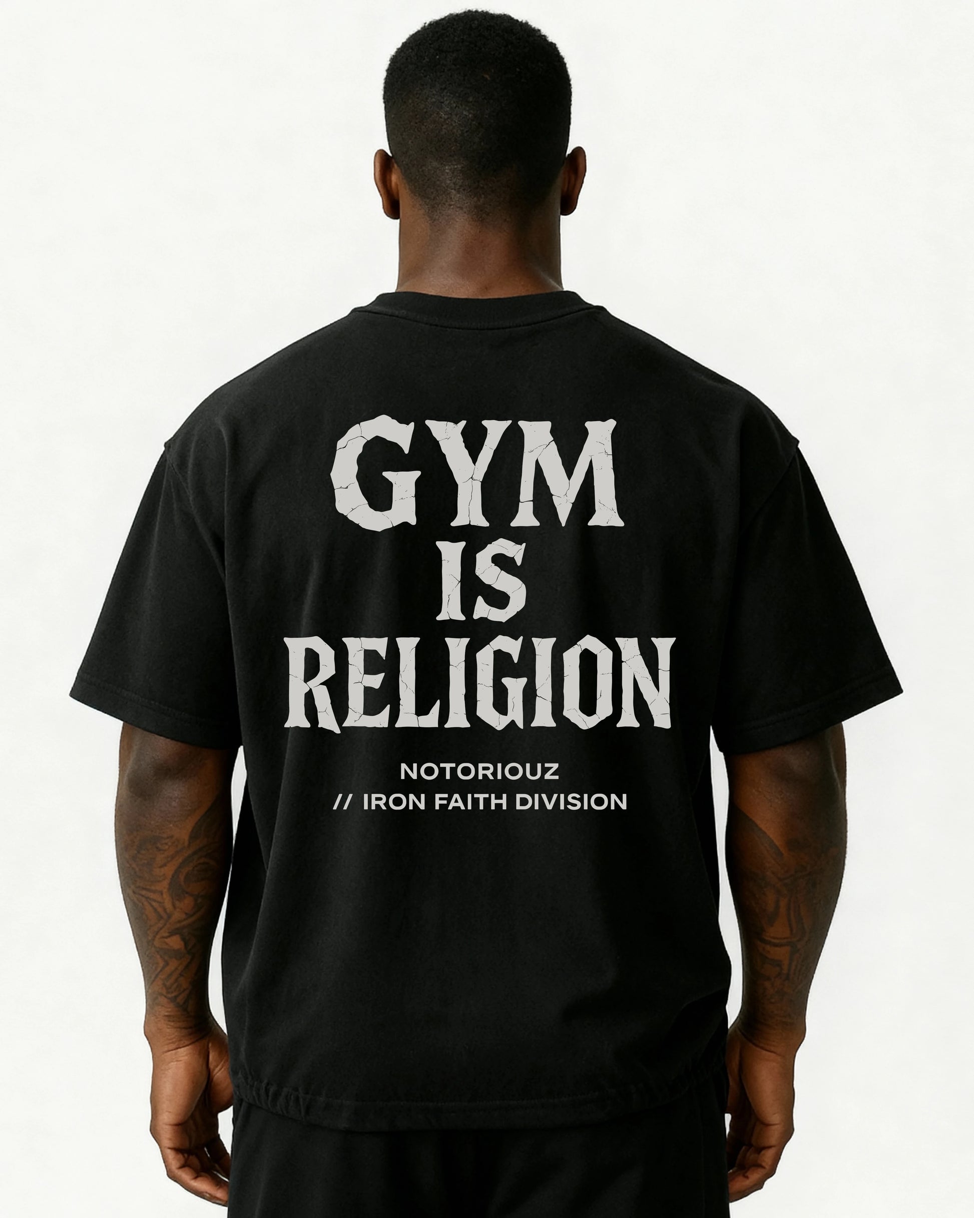 “Oversized T-Shirt in Schwarz mit großem Rückenprint: weißer Schriftzug ‚GYM IS RELIGION‘ im Stein-/Crack-Stil, darunter ‚Notoriouz // Iron Faith Division‘. Getragen von einem athletischen Mann, Rückenansicht.“