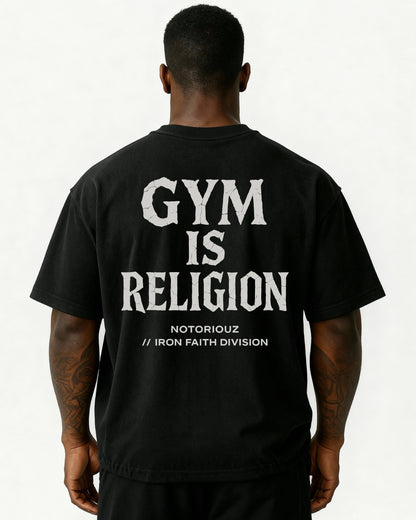 “Oversized T-Shirt in Schwarz mit großem Rückenprint: weißer Schriftzug ‚GYM IS RELIGION‘ im Stein-/Crack-Stil, darunter ‚Notoriouz // Iron Faith Division‘. Getragen von einem athletischen Mann, Rückenansicht.“
